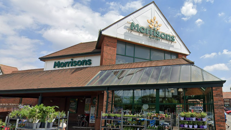 Një pamje e dyqanit Morrisons, një strukturë me tulla dhe xham, me rafte me plane përpara hyrjes. Të drejtat e autorit.