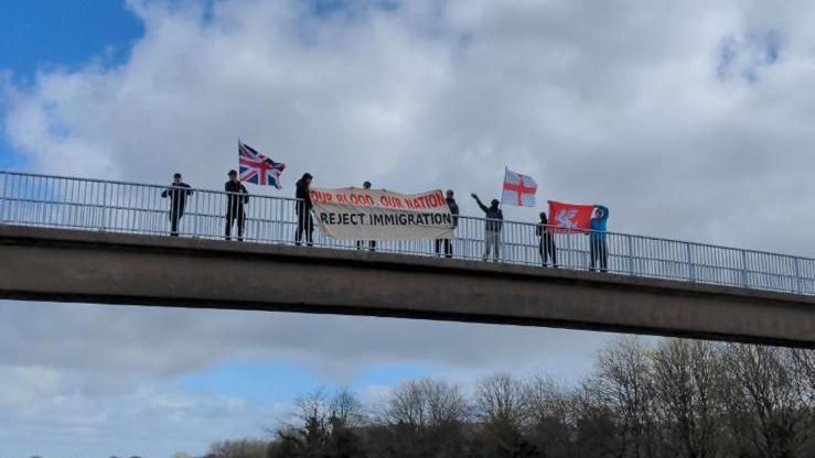 Eight Active Club members hold a racist banner over a motorway flyover near Liverpool 