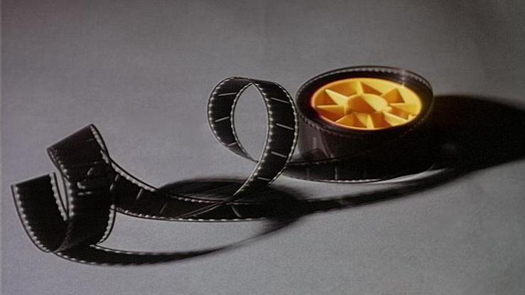 A roll of 35mm film on a yellow reel - some has unwound from the reel and is curled up and lying next to it.