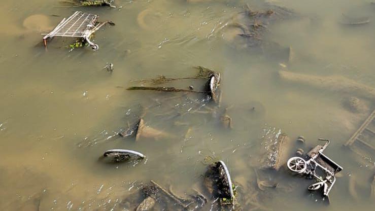 Rubbish items in the River Parrett. A shopping trolley and a tricycle are visible in the water, which is  a muddy brown colour