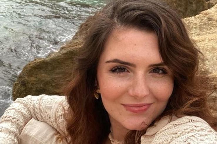 Hannah-Lucy Jackson is smiling at the camera, she has brown wavy hair and is wearing a cream cardigan.