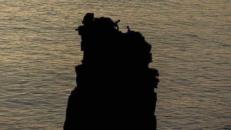 Climbers silhouetted against the sea on the rocky sea stack Am Buachaille