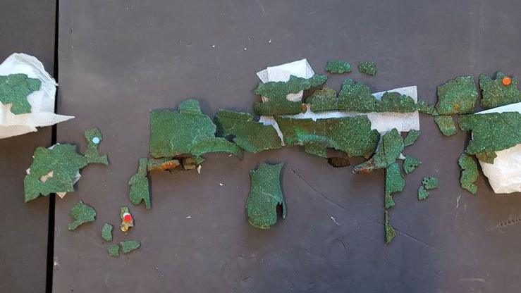 Fragments of an Iron Age helmet laid out upon a table. The copper sheeting has gone green over the centuries. Some are curved. They are laid out in the order they would have gone in, if the helmet was intact.