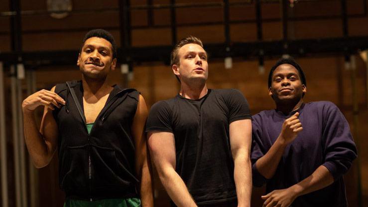 Three actors move their bodies in a rehearsal. They are all pulling different poses as if dancing.