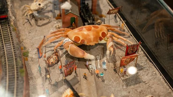 A model of a giant orange crab with red spots towering above miniature figures of people at Crab Museum in Margate 