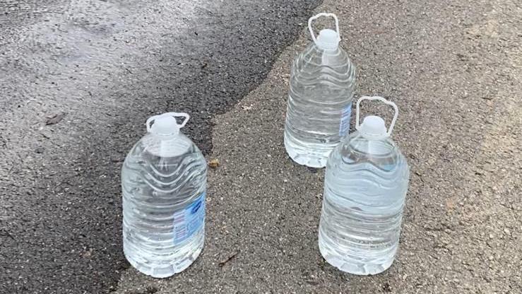 Plastic bottles full of water, beside a road where flood water is flowing.down