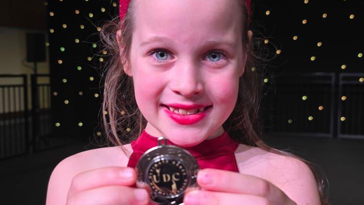 Beatrice holding a medal at a competition. She is wearing a red dress and smiling. 