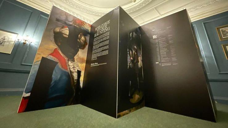 A cardboard banner detailing the contents of the exhibition. The picture of a black man dressed according to the time period is featured on the left.