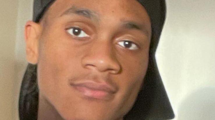 A close up of the face of a young man. He has brown eyes and is clean shaven.