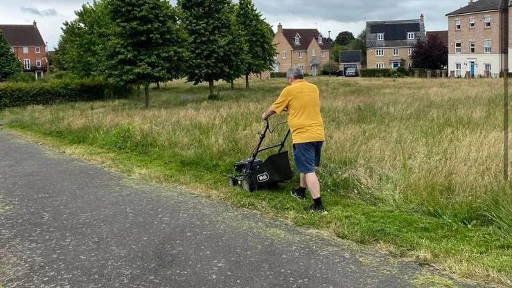 Derby resident Russell Armstrong mowing overgrown grass outside a residential estate, yellow polo shirt blue shorts