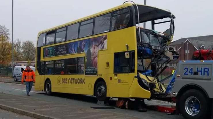 A yellow double decker bus with a destroyed front, being towed by a recovery vehicle.