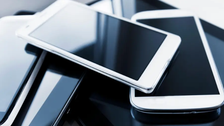 A pile of mobile phones sitting on top of each other. The screens are all blank.