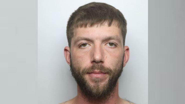 Custody photo of Oswald. He has dark hair and a beard.