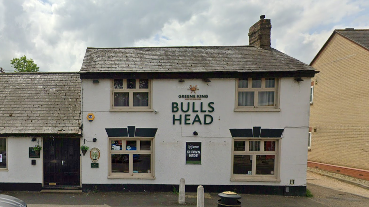 A white building with "The Bulls Head" in large letters in the centre alongside a Greene King logo. The image is from 2023.