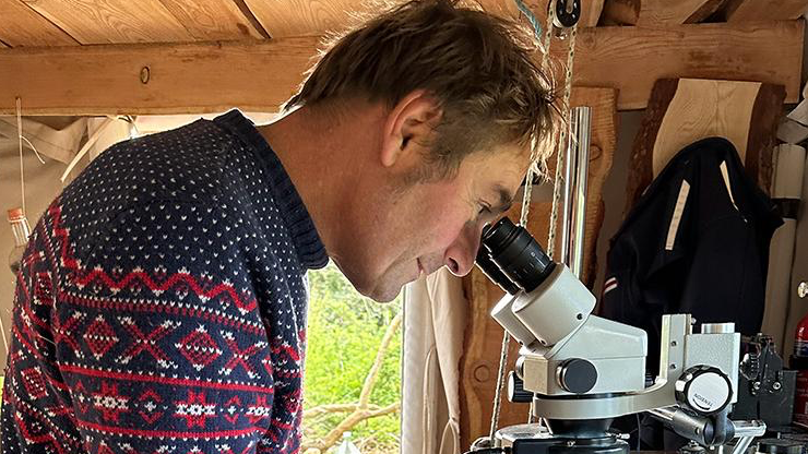 Bart Sabel looks through a microscope inside The Gingerbread House. The picture is a side view of Mr Sabel and he's wearing a navy and red woollen jumper.