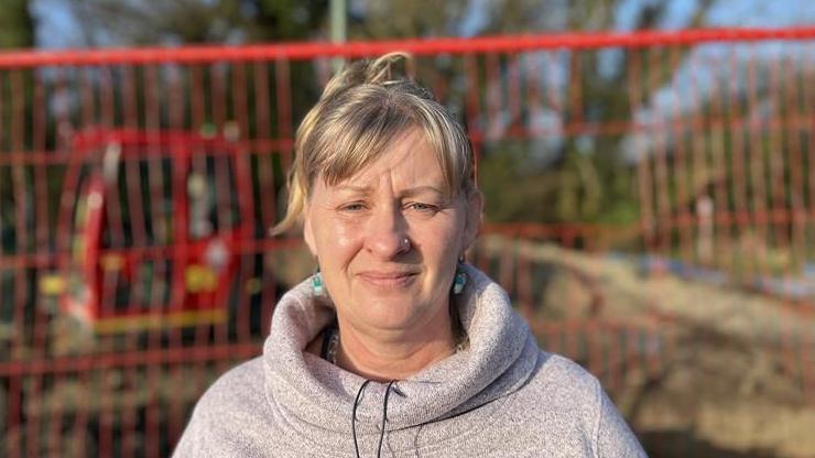 A woman in a pink jumper stood in front of a building site with a red fence