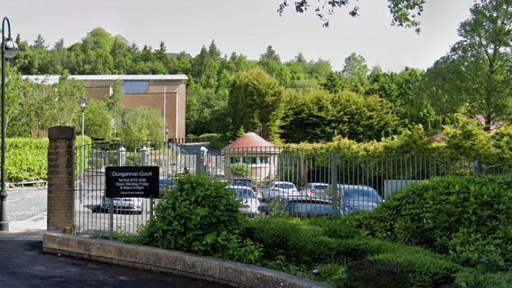 A carpark with a grey railing in front of it. In front of the railing is a row of green bushes and a black sign reading Dungannon Court. 