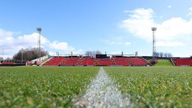 A view of Gateshead International Stadium with two floodlights above an open air stand that has 'GMBC' painted in black on red seats.