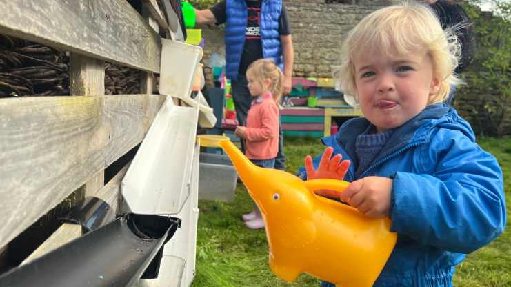 A small boy wearing a blue coat holding a yellow watering can