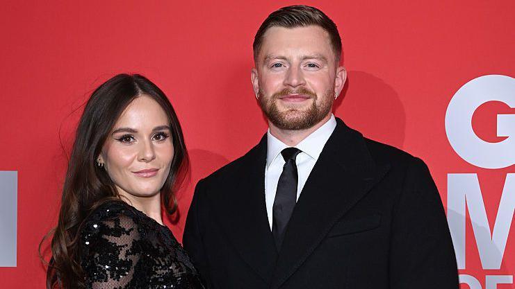 Holly Ramsay and Adam Peaty in front of a red backdrop