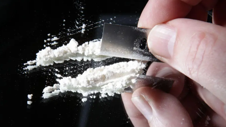 A hand cutting white powder with a blade on a mirrored surface