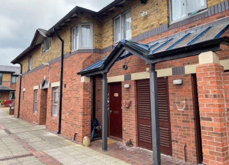 A two-tone brick-built house with wooden doors and shutters and a glazed canopy.