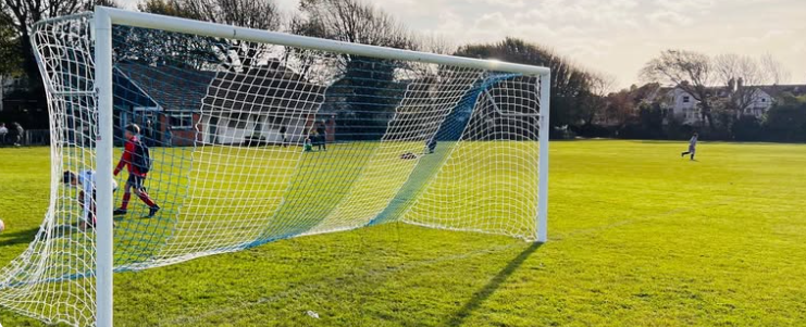 Goalposts on a football pitch with two children and an adult in the background.