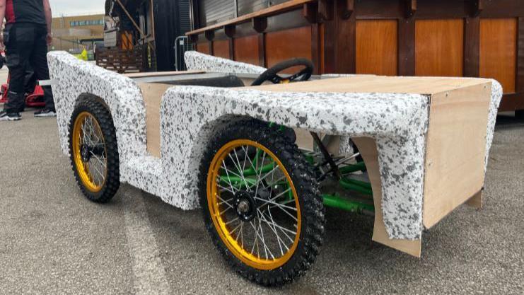 A white and black speckled soapbox cart with w with big black and yellow wheels