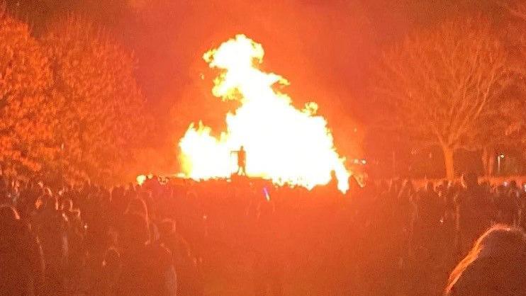 A crowd in front of a large bonfire.