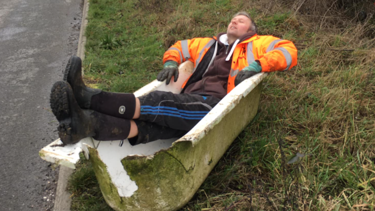 A man lying in a broken bath dumped at the side of the road