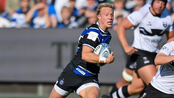 Sam Harris runs with the ball tucked under his right arm during a match as Bristol Bears players run alongside him