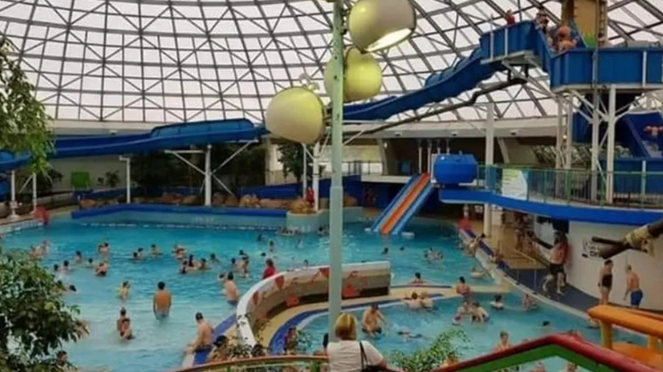 Oasis leisure pool in action, with various slides and many people playing in the water. The famous domed roof with its metalwork lattice sits atop.