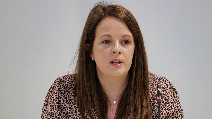 Nuala McAllister sitting down, she has long brown hair and is wearing a blouse with a leopard print type design