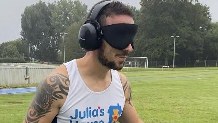 Top half of Alex Bance running with a Julia's House t-shirt, ear defenders and an eye mask