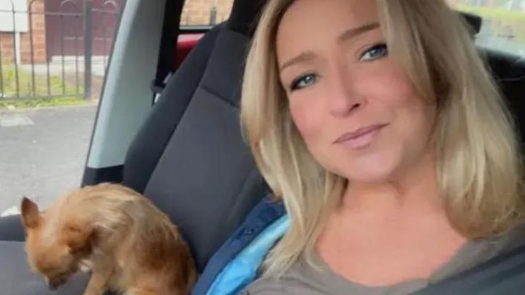 Teresa McMahon, with long blonde hair and blue eyes, smiles as she sits in a car alongside a chihuahua dog.