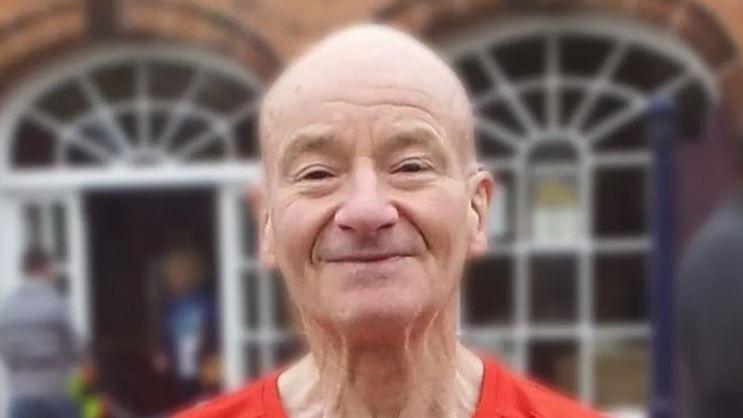 An elderly man smiles at the camera wearing a red-t-shirt