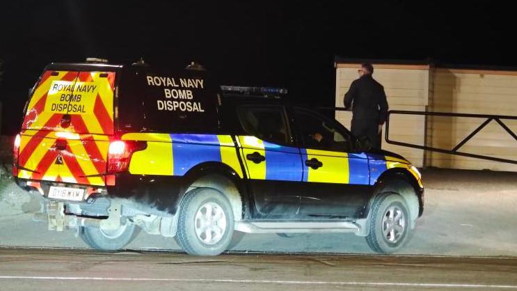 A Royal Navy bomb disposal vehicle parked at a beach at night