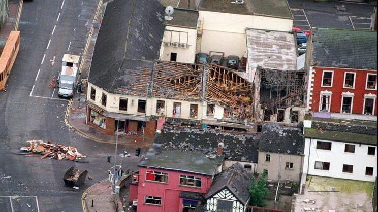 An aerial view of the 1998 Omagh bomb scene supplied by the Ministry of Defence.  It shows several badly damaged buildings at the corner of Market Street.  Some of the roofs have collapsed and there are piles of broken furniture and wood in the middle of the junction.