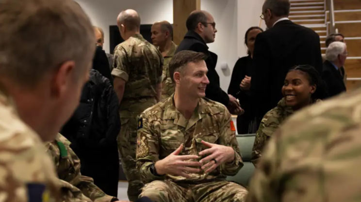 Individuals chatting, at the centre of the image is a man and a women. They are both wearing camouflage Army uniform. 