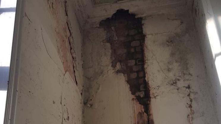 A corner of the building inside which shows exposed brick and crumbling paintwork. 