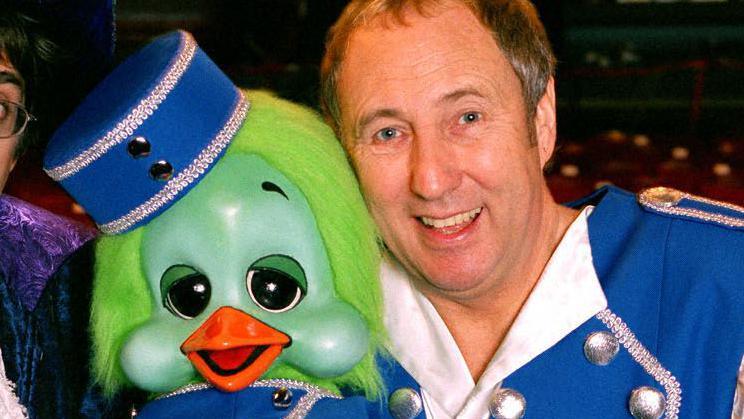 Keith Harris, in a blue and white stage costume for the Cinderella character Buttons and holding Orville, his green puppet duck