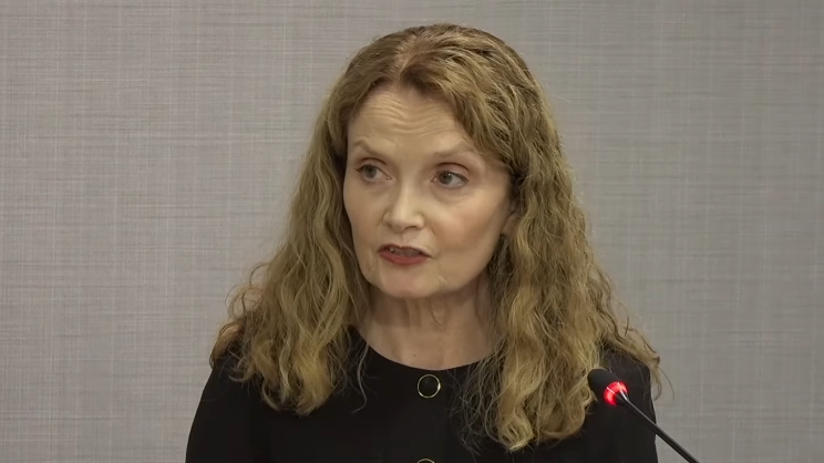 Una Doherty KC, a woman with shoulder-length blonde hair and a black top speaks into a microphone