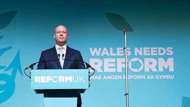 Reform UK's Dan Thomas standing behind a Reform UK branded podium.