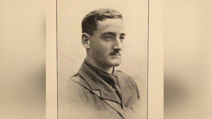 A sepia photograph from the early 1900s shows a three-quarter profile of a man. He has short hair and a neat moustache and is wearing what appears to be some form of a uniform.