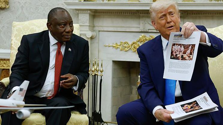 President Donald Trump holds up a printed article from American Thinker while accusing South Africa President Cyril Ramaphosa, who is seated next to him, of state-sanctioned violence against white farmers in South Africa in the Oval Office at the White House on 21 May 2025 in Washington DC.