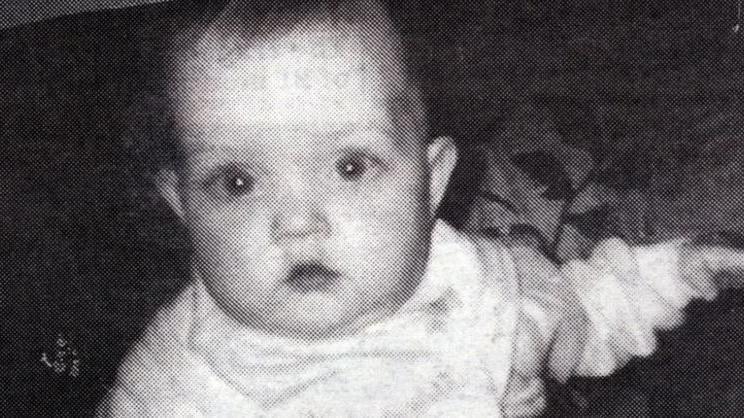 A little girl looks into the camera. She is wearing a light coloured outfit. The picture is black and white.