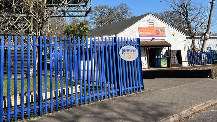 Outside of the Alpine Snowsports Centre in Aldershot on a sunny day. There is a sign for Rushmoor Borough Council on the blue fence.