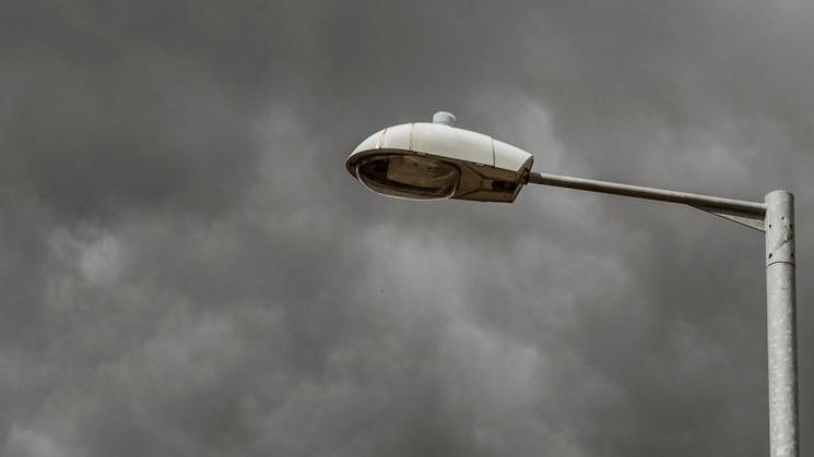 A close up of a street light against a very cloudy sky.