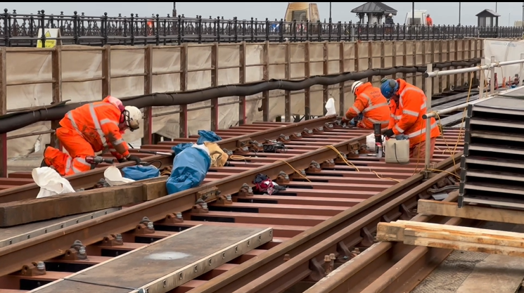 Several engineers working on the railway track in orange work overalls.