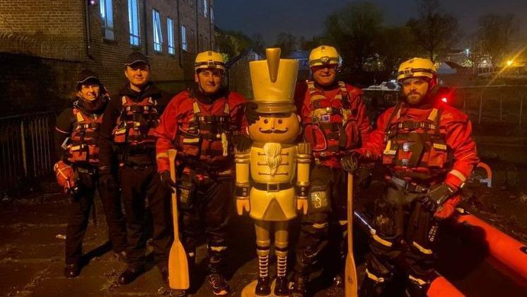 Divers and police officers in nighttime by the river Foss in York, posing with "nutcracker" figure dressed in a soldier's uniform